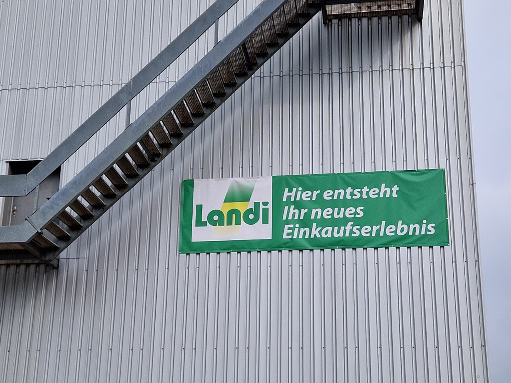 Banner der Landi an einer Metallfassade im Vitus-Areal Winterthur, das auf ein neues Einkaufserlebnis hinweist.