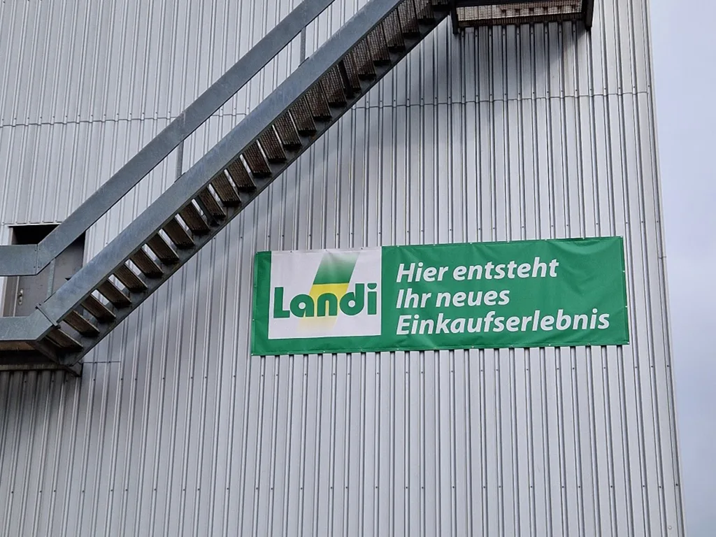Banner der Landi an einer Metallfassade im Vitus-Areal Winterthur, das auf ein neues Einkaufserlebnis hinweist.